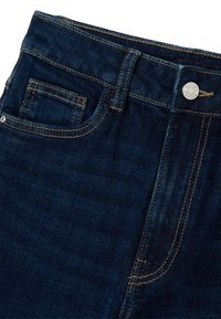 Jeans de mezclilla azul oscuro con un diseño elegante. Cuenta con un bolsillo frontal, costuras visibles y un botón de metal en la cintura.