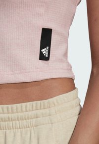 Top corto de canalé rosa claro con una etiqueta negra de Adidas. Pantalones con cintura elástica en color beige y costuras visibles. Enfoque en texturas y colores.