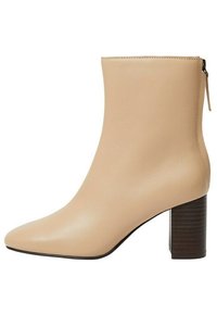 Botín de cuero beige hasta el tobillo con punta afilada y tacón marrón estriado. Cuenta con un cierre de cremallera lateral para facilitar su uso. Textura suave.