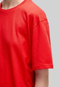 Rotes Baumwoll-T-Shirt mit rundem Halsausschnitt und kurzen Ärmeln. Der Stoff hat eine glatte Textur, mit minimalen Nähten und ohne sichtbare Muster.