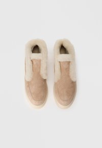Bež zamšaste papuče s mekanim kremastim krznom unutar i na rubovima, slip-on stil, prikazane na jednostavnoj bijeloj pozadini.