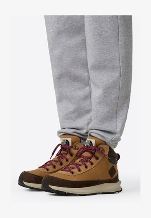 Barna túrabakancs bordó fűzőkkel, mintás vászon felsőrésszel és gumitalppal, szürke melegítőnadrággal párosítva.