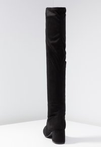 Botas negras de gamuza sobre la rodilla, con un tacón grueso y una textura suave, con mínimos detalles de costura.