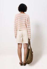 Leichtes Strickoberteil mit rosa-weißen Streifen, kombiniert mit cremigen Shorts. Hält eine hellbraune Umhängetasche im Leopardenmuster. Lässiges Ensemble.
