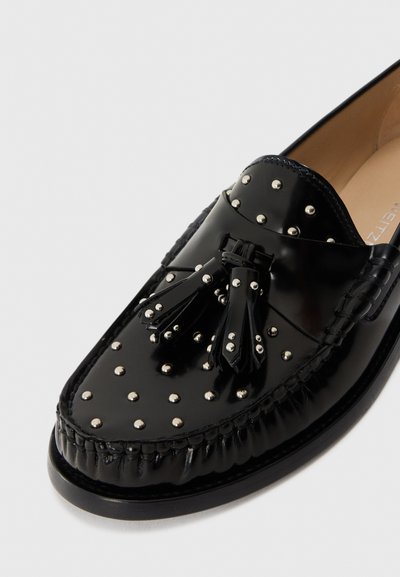 Mocassins en cuir verni noir, ornés de clous argentés, d'une texture tissée et de franges, avec un bout rond et des détails de couture contrastants.