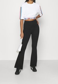 Bílý zkrácený tričko s modrými a červenými pruhy na rukávech a logem; černé zvonové kalhoty; černé sportovní boty s bílými pruhy; bílá taška.