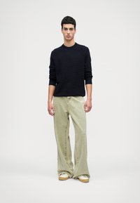 Ναυτικό πλεκτό πουλόβερ με κανονική λαιμόκοψη, σε συνδυασμό με ανοιχτόχρωμα πράσινα παντελόνια με φαρδύ πόδι και μπεζ παπούτσια με χρυσή λεπτομέρεια.