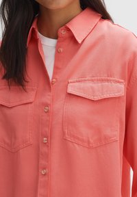 Korallenrotes Hemd zum Knöpfen mit Kragen, zwei Brusttaschen und einer strukturierten Stoffoberfläche. Weiches Finish und leichte Ziernaht-Details.