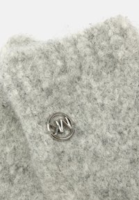 Tejido de punto texturizado gris con acabado borroso; presenta un adorno redondo de metal plateado con iniciales en el centro.