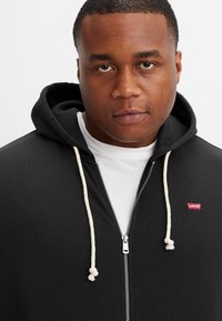 Zwarte zip-up hoodie van katoen, met een witte trekkoord, zilveren rits en een klein rood Levi's logo op de linkerkant van de borst.