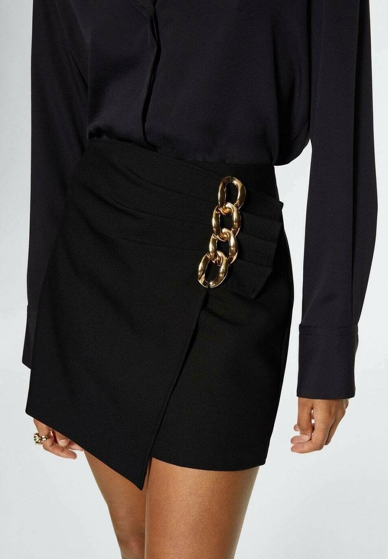 Sort mini-nederdel med asymmetrisk design, der har en gylden kædeaccent på siden og struktureret stof for ekstra detaljer.