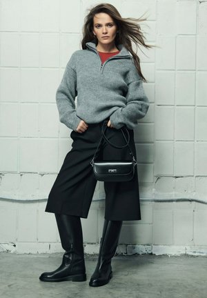 Szary sweter prążkowany z kołnierzem na zamek, czarne kuloty, czarne kozaki za kolano oraz mała czarna torebka ze srebrnymi elementami.