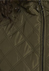 Veste matelassée vert olive avec une fermeture éclair à l'avant, des boutons ronds en métal et une surface texturée avec un motif en losange.
