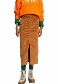 Jupe midi en velours côtelé marron avec une fente frontale, associée à un sweat à capuche orange vif et des bottines crème. Accents verts sur les manches et les chaussettes.