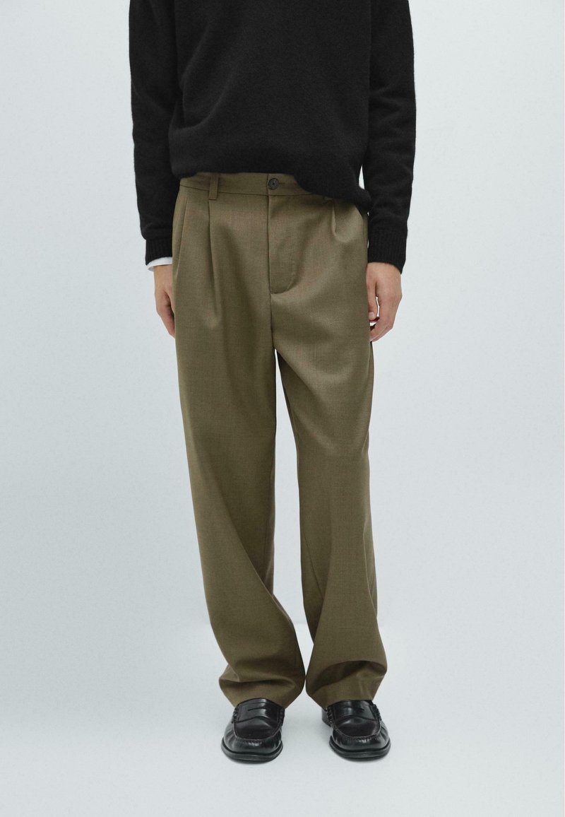 Khaki pleated trousers made of lightweight fabric, featuring a regular fit, button closure, and smooth texture. Black shoes complete the look.