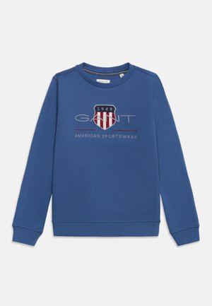 Sweat-shirt bleu à manches longues avec col rond, logo GANT, emblème en forme d'écu avec l'inscription "1949" et texte "American Sportswear" sur la poitrine.