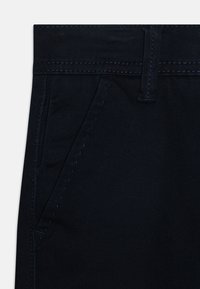 Mørkeblå bukser laget av en bomullsmiks, med en jevn tekstur, synlige sømmer og sidelommer. Minimalistiske designdetaljer.