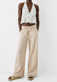 Lichtgewicht haltertop met een gerimpelde taille en een trekkoorddetail, gecombineerd met wijde beige broeken met zijzakken.