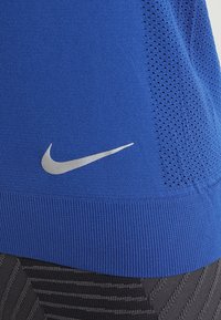Top atlético azul hecho de una tela suave, con una sección de malla texturizada, dobladillo acanalado y un logo de Nike plateado en la parte frontal.