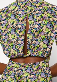 Robe à motifs floraux avec un fond noir et des fleurs multicolores en vert, violet et beige ; comprend un détail en découpe dans le dos.