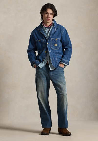 Τζιν μπουφάν με δύο μπροστινές τσέπες, μπλε χρώμα, σετ με ανοιχτόχρωμο πουκάμισο τζιν και ξεθωριασμένο μπλε τζιν παντελόνι. Καφέ σουέντ μποτάκια. Ουδέτερο φόντο.