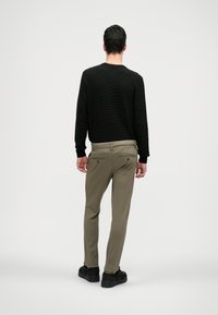 Svart texturerad tröja och olivgröna byxor. Byxorna har bakfickor och är tillsammans med svarta sneakers för en avslappnad look.