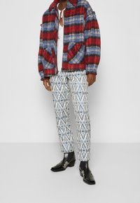 Giacca a quadri multicolore con sfumature rosse, blu e nere; abbinata a pantaloni bianchi con motivi geometrici; stivali in pelle nera.