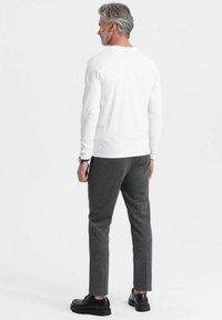 Weißes langärmliges Hemd, graue Hose und schwarze Schuhe. Das Hemd hat eine glatte Textur, während die Hose aus einem weichen, dickeren Stoff gefertigt ist.