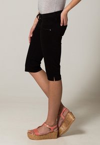 Pantalons capri noirs à mi-mollet avec fentes latérales, associés à des sandales compensées pêche avec détails tressés et brides autour de la cheville.