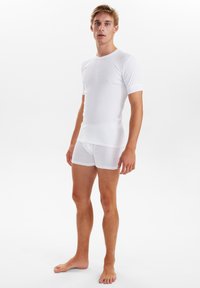 Hvid t-shirt med korte ærmer lavet af blødt materiale, parret med hvide boxershorts, begge med et enkelt design og glat tekstur.