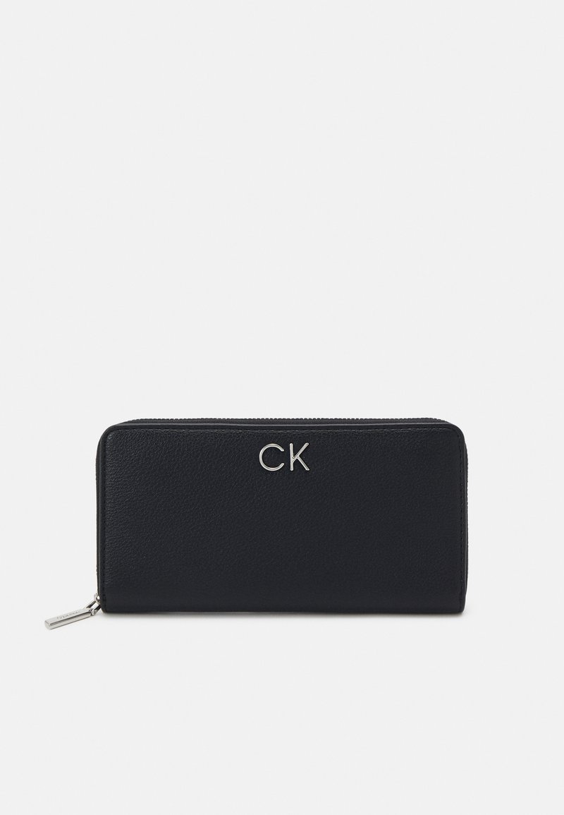 Portafoglio in pelle nera con logo "CK" in argento, chiusura con zip, forma rettangolare, superficie texturizzata e design minimalista.
