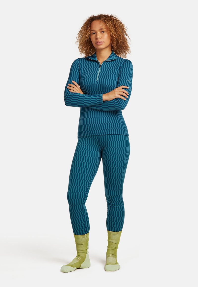 Zestaw odzieży sportowej składający się z tealakowego topu w wzory z kołnierzem na pół suwak i dopasowanych legginsów. Uzupełniony jasnopistacjowymi skarpetkami.