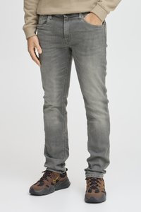 Jeans gris ajustados con una textura suave, cinco bolsillos y un lavado sutil. Combinados con zapatillas marrones y negras con un acento amarillo.