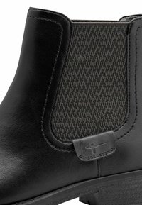 Botte Chelsea en cuir noir avec panneau latéral élastique texturé et petite languette en cuir au-dessus de la semelle.
