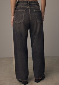 Jeans de pierna ancha de lavado oscuro con una cintura alta, que presentan dos bolsillos en la parte posterior y un largo recortado. La tela tiene una textura desvanecida.