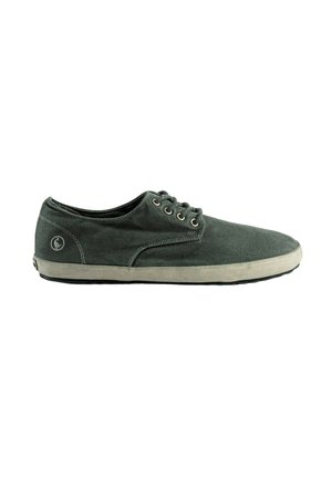 Zapatilla informal de lona gris oscuro con suela de goma blanca y cordones en la parte delantera, mostrada de perfil sobre un fondo blanco.