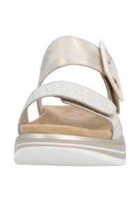 Sandales blanches avec une bride à motif, une tige en métal doré, une semelle intérieure texturée et une boucle ronde blanche. Elles présentent une semelle basse et rembourrée.