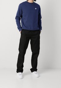 Tmavě modrá mikina Nike s kulatým výstřihem a bílým logem, doplněná černými pohodlnými kalhotami a bílými teniskami.