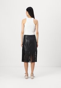 Fekete bőrszoknya bojt részletezéssel az alján, fehér pántos felsővel párosítva. Simás textúra és közepes hosszúságú kialakítás.