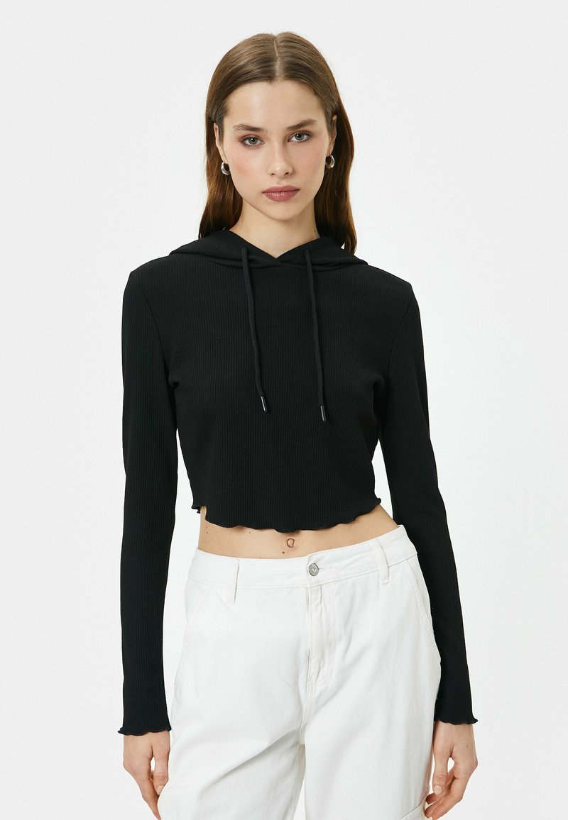 Sudadera corta negra con textura acanalada, mangas largas y un dobladillo ondulado. Presenta una capucha con cordón y un acabado de tela suave.