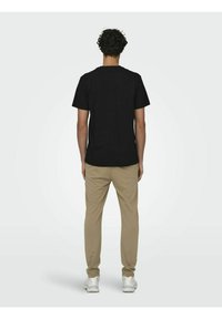 Camiseta negra de manga corta combinada con pantalones beige claros, vista desde atrás. Diseño simple, textura suave y ajuste estándar.