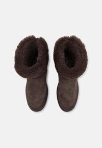 Brune ankelstøvler i ruskind med en blød, fluffy foring øverst. Rund tåform og tekstureret overflade. Gummisål for godt grep.