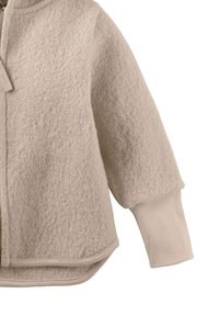 Beige strukturierte Fleecejacke mit geripptem Ärmelbund und abgerundetem Saum auf einem weißen Hintergrund.