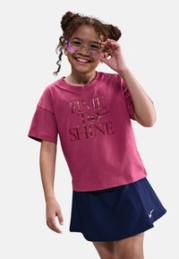 Camiseta de algodón rosa con gráfico de "TIME TO SHINE", combinada con una falda plisada azul marino que presenta un logo. Niño usando gafas.
