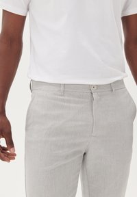 Jasnoszare spodnie z teksturowanej tkaniny, z zapięciem na guzik i bocznymi kieszeniami. W komplecie z białym t-shirtem z krótkim rękawem.