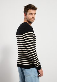 Suéter a rayas en colores negro y crema, con textura acanalada en los hombros, cuello redondo y diseño ajustado. Combinado con jeans de color azul claro.