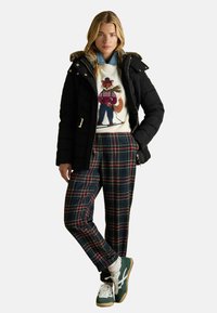 Melnā pūkainā jaka ar kažokādu apdari, balta džemperis ar lapsu motīvu un jūras zila pludmales svārki. Zaļa apavi ar brūnu zoli noslēdz apģērbu.