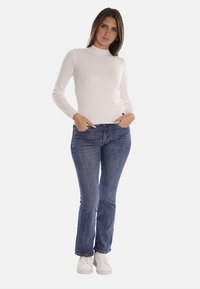 Maglione bianco a collo alto, design aderente, abbinato a jeans blu, taglio dritto, denim testurizzato, indossato con sneakers bianche.