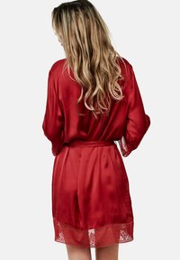Robe en satin rouge avec une finition en dentelle au niveau de l'ourlet. Présente une taille à nouer et des manches amples, mettant en valeur une texture lisse et glossy.