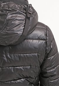 Černá prošívaná péřová bunda s velkou kapucí a nastavitelným popruhem na zadní straně.